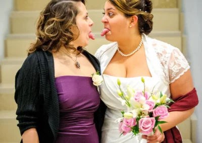 Braut mit Brautjungfer lacht auf Treppe, Hochzeitsfoto nahe Dillingen, zeigt Froehlichkeit und Freundschaft.