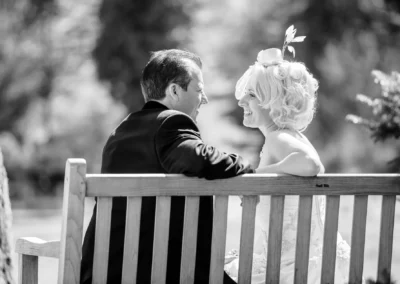 Brautpaarfoto auf Holzbank im Kurpark Bad Toelz, festgehalten von Hochzeitsfotograf in natuerlichem Licht.