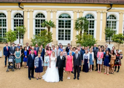 Gruppenfoto bei einer Hochzeit vor der Orangerie Ansbach. Brautpaar und Gaeste posieren fuer ein Hochzeitsfoto.
