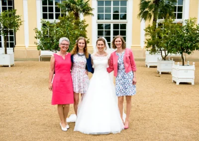 Braut mit drei Frauen vor der Orangerie Ansbach bei einer Hochzeitsreportage umgeben von Gruenpflanzen.