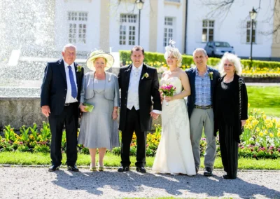 Hochzeitsfoto von einem Brautpaar mit Familie im Kurhaus Bad Toelz, sonniger Tag, Blumen im Hintergrund.