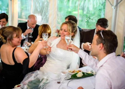 Braut und Gaeste beim Anstossen, lachend im Zelt bei Hochzeit in Schwabing, Muenchen. Hochzeitsfotograf dokumentiert.
