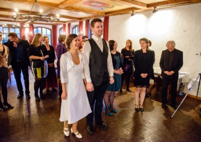 Brautpaar lacht mit Gästen in einem Raum beim alten Wirt in Grünwald. Hochzeitsreportage zeigt Freude des Moments.