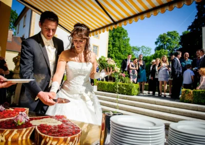 Brautpaar schneidet Hochzeitstorte unter Pavillon im Schloss Aufhausen bei Erding vor versammelter Hochzeitsgesellschaft.