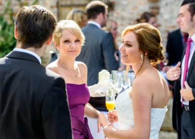Braut mit Sektglas lacht neben Gaesten im Freien bei einer Hochzeit in Landshut, festgehalten in Hochzeitsfoto.
