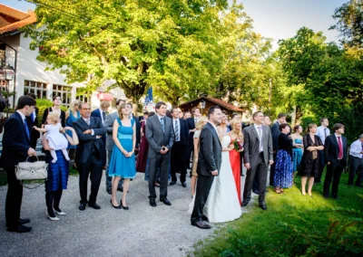 Hochzeitsgesellschaft nahe dem Ammersee bei einer Hochzeit, festlich gekleidete Gaeste unter Baeumen im Freien.