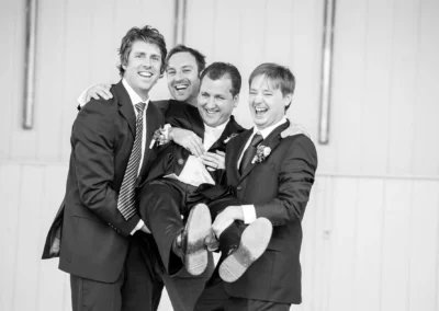 Männer in Anzügen lächeln und tragen Bräutigam bei Hochzeit in Bad Toelz, Hochzeitsfotografie in Oberbayern.