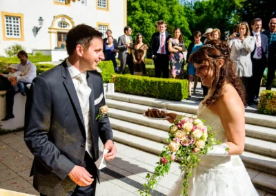 Hochzeitsreportage bei Schloss Aufhausen: Braut und Bräutigam beim Tortenanschneiden, umgeben von Gästen im Garten.