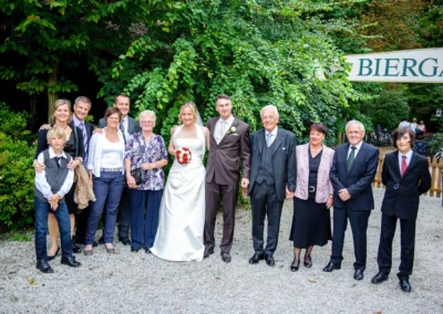 Brautpaar mit Familie und Freunden bei einer Hochzeitsfeier im Biergarten in Schwabing. Elegant gekleidet im Freien.