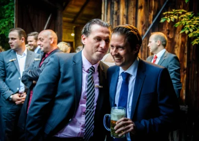 Zwei elegant gekleidete Maenner in Anzuegen bei Hochzeit in Eventscheune Wallenburg, einer haelt ein Bierglas.