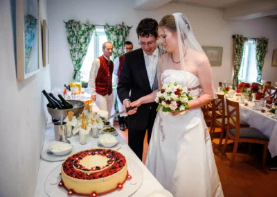 Brautpaar schneidet Hochzeitstorte bei Hochzeit in Muenchen. Hochzeitsfotografie im Fokus, festlicher Moment eingefangen.