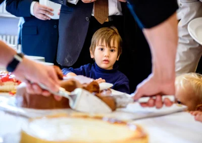 Kleinkind beim Schneiden von Hochzeitstorte, begleitet von Erwachsenen, auf einer Hochzeit bei Schloss Gruenau.