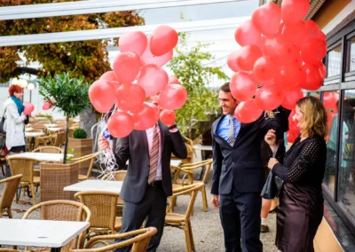 Gäste mit roten Ballons auf einer Hochzeit am starnberger see, Hochzeitsfotografie mit fröhlichen Momenten im Freien.