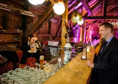 Barkeeperin schenkt Bier bei Hochzeit in Eventscheune Wallenburg ein, Miesbach. Hochzeitsfoto in festlicher Stimmung.
