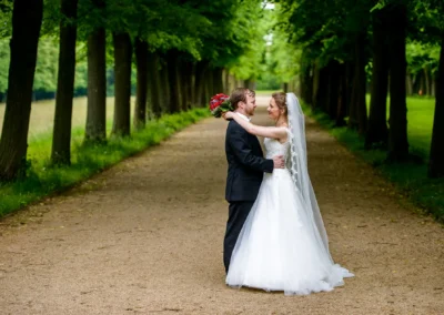 Brautpaar bei Hochzeitsportrait im Hofgarten Ansbach, posierend auf von Bäumen gesäumtem Weg. Hochzeitsfotografie.