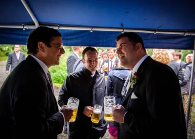 Gäste genießen Bier auf Hochzeit in Miesbach, unter Pavillon stehend. Fröhliche Atmosphäre der Hochzeitsreportage.