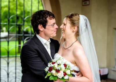 Brautpaar lacht und umarmt sich, sie traegt Schleier, er Anzug. Hochzeit in München, Schloss Blutenburg.