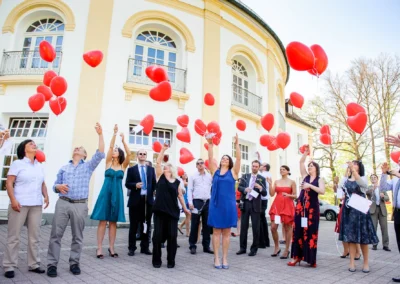 Hochzeitsfoto im Kurhaus Bad Toelz: Menschen lassen rote Herzballons steigen bei sonniger Feier. Hochzeitsreportage.