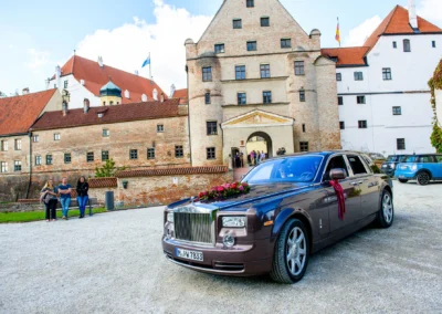 Luxusauto geschmückt für Hochzeit bei Burg Trausnitz, im Hintergrund historisches Gebäude aus Ziegelstein.
