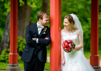 Brautpaar im Hofgarten Ansbach, lachend unter roter Pergola, Hochzeitsfoto in natuerlicher Kulisse.