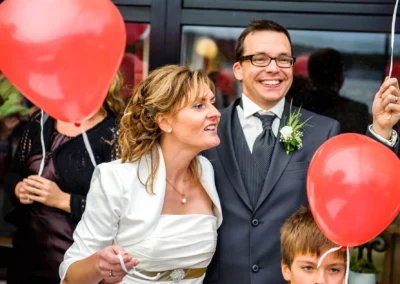 Brautpaar mit roten Ballons bei der Hochzeit am Starnberger See, Hochzeitsfotografie in lebendiger Szene eingefangen.