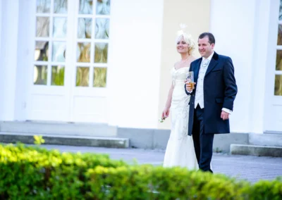 Brautpaar bei Hochzeit vor Kurhaus Bad Toelz. Er laechelt, sie traegt weisses Kleid und er dunklen Anzug. Hochzeitsfoto.