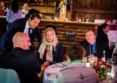 Gäste sitzen an einem Tisch bei einer Hochzeitsfeier in der Eventscheune Wallenburg, mit Blumen und Kerzen dekoriert.