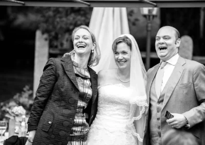 Glückliches Brautpaar lacht neben Gast bei Hochzeit in Aying, festgehalten von Hochzeitsfotograf im Landkreis München.