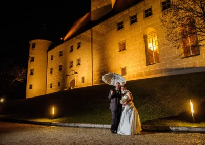 Brautpaar bei Nacht vor Schloss Hochstadt an der Donau, romantisches Hochzeitsfoto mit Regenschirm und Beleuchtung.