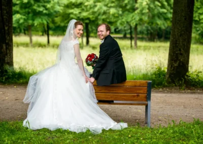 Brautpaar sitzt auf einer Bank im Hofgarten Ansbach. Hochzeitsfotografie im Gruenen.