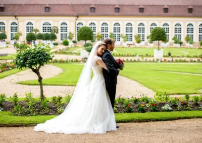 Brautpaar bei Hochzeitsportrait im Hofgarten in Ansbach stehen umarmt vor historischer Kulisse und Blumenrabatten.