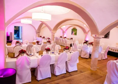 Elegante Hochzeitsdekoration in einem Saal mit gewoelbter Decke im Augustlhof Pfettrach. Hochzeitsfoto am Tisch.