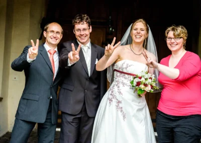Vier lachende Personen posieren bei einer Hochzeitsreportage in Schloss Blutenburg. Braut mit Blumenstrauss.