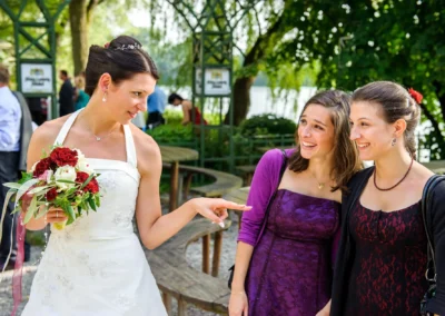 Braut in weissem Kleid mit Blumenstrauss spricht mit zwei Frauen bei Hochzeit am Langwieder See, Hochzeitsfoto.