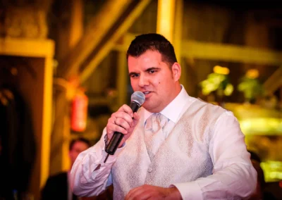 Redner bei Hochzeit in Eventscheune Wallenburg, elegant gekleidet, mit Mikrofon. Hochzeitsreportage aus Miesbach.