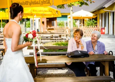 Braut mit Blumenstrauss laechelt zwei Damen an, aufgenommen bei einer Hochzeit westlich von Muenchen.