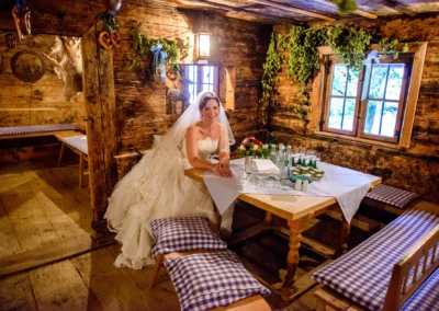 Braut in rustikaler Stube in Brauereigasthof Aying, bei Hochzeitsreportage im Landkreis München, lächelnd am Tisch.