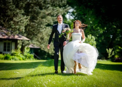 Brautpaar laeuft lachend ueber eine Wiese in Schloss Aufhausen bei Erding, Hochzeitsfoto voller Freude und Bewegung.