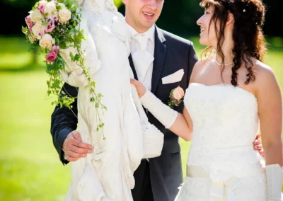 Brautpaar lacht neben einer weissen Statue im Schloss Aufhausen. Hochzeitsfotografie nahe Muenchen.