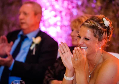 Braut laechelnd beim Applaus auf Hochzeit in Miesbach, Hochzeitsfotograf haelt Moment fest, rosa Hintergrund.