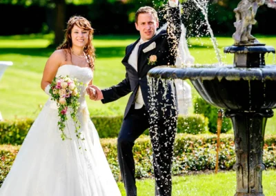 Brautpaar lacht neben einem Brunnen bei Schloss Aufhausen, festgehalten bei einer Hochzeitsreportage nahe Muenchen.
