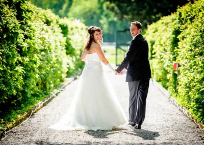 Brautpaar beim Hochzeitsshooting im Schloss Aufhausen, spazierend auf einem Kiesweg umgeben von gruenen Bueschen.