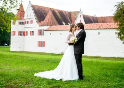 Brautpaarfoto vor Schloss Gruenau, Hochzeit in Neuburg an der Donau. Brautpaar laechelnd, gruenes Gras im Vordergrund.