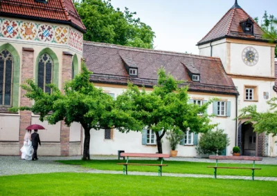 Brautpaar mit Regenschirm vor Schloss Blutenburg in Muenchen. Hochzeitsfotografie bei einer Hochzeit.