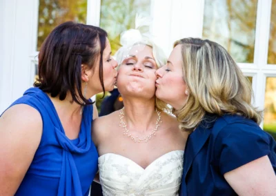 Braut in weissem Kleid wird bei Hochzeit von zwei Frauen auf die Wangen gekuesst, aufgenommen in Bad Toelz.