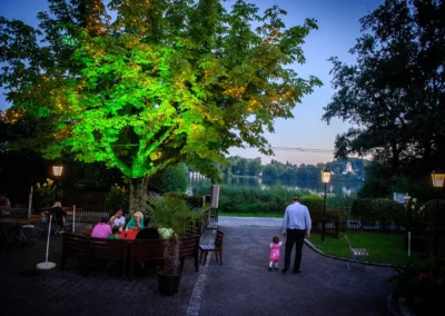 Paar im Gartenrestaurant bei Hochzeit nahe Wesslinger See, Hochzeitfotografie mit See im Hintergrund und beleuchtetem Baum.