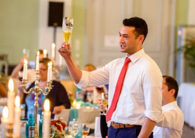 Mann im Hemd und roter Krawatte erhebt Glas zum Trinkspruch bei Hochzeit in der Orangerie Ansbach.