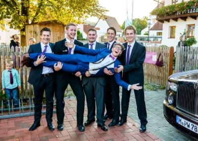 Junggesellen tragen Bräutigam bei Hochzeit in Landshut, alle in Anzügen, posieren fröhlich für Hochzeitsfotograf.