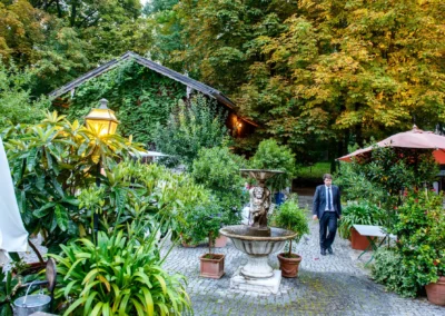 Gartenanlage bei Hochzeit im Brauereigasthof Aying mit beleuchteter Laterne, Brunnen und Mann im Anzug