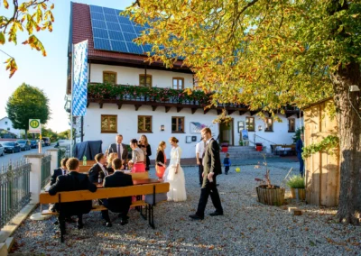 Hochzeitsfoto in Landshut: Brautpaar mit Gästen vor einem Haus mit bayerischer Fahne im Garten unter Bäumen.
